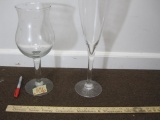 2 oversized glass holders, 13 inches tall and 16 inches tall, one shaped like a wine flute