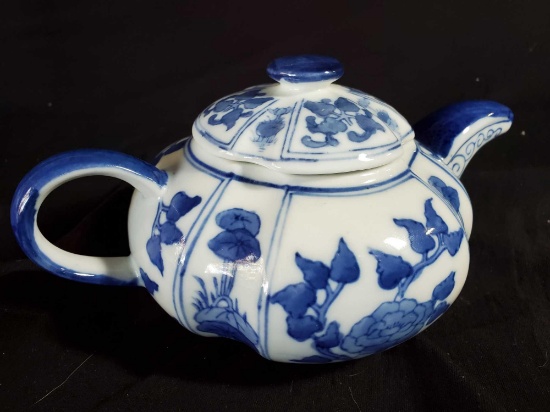 A blue and white porcelain teapot painted with flowers and lilly pads