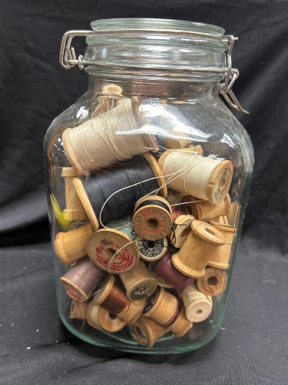vintage Crown canning jar filled with a collection of old wooden spools of thread