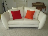 White Leather Loveseat w/Red & Orange Accent Pillows.  Some pricks on arms.