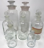 Eight clear pharmacy/medicine bottles missing one lid