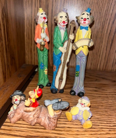 Three tall clowns clown, laying on his belly with one on his back one small clown playing as cymbals