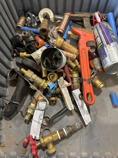 Tote with various items such as pipe wrench, brass fittings, hole saw and more