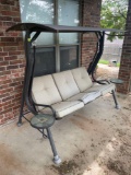 Porch swing with umbrella cover and attached side tables, needs new cushions. Please bring help to