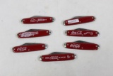 Seven Coca-Cola advertising knives with 2.5 inch single blades and red scales.