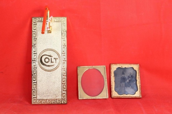 Gold colored metal Colt pistol barrel display rack and two small gold colored picture frames.