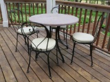 Outdoor bistro table with stone top and four metal chairs with cushions