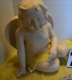 Baby White Ceramic Angel sitting on ground wearing a yellow shad across body with eyes closed