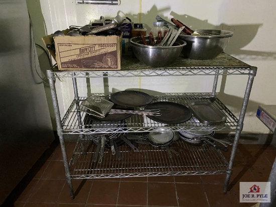 Metal rack with contents: cooking utensils, stainless steel bowls, skillets, etc