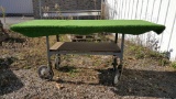 INDUSTRIAL-STYLE GURNEY CART WITH WOODEN TOP AND OUTDOOR CARPET. RUBBER IS