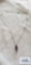 Silver colored pendant with purple gemstone and clear gemstones on silver colored chain, both marked