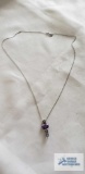 Silver colored pendant with purple gemstone and clear gemstones on silver colored chain, both marked