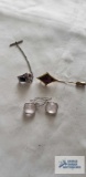 Gold colored pin with purple stone, silver colored tie clip with blue stone, and pale pink earrings