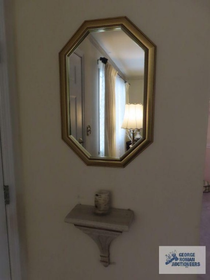 Wall shelf with candle sconces, candle with candle holder, and gold framed wall mirror