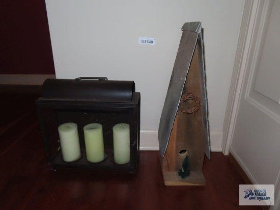 Wooden birdhouse with slate roof. Metal and glass candle holder with candles.