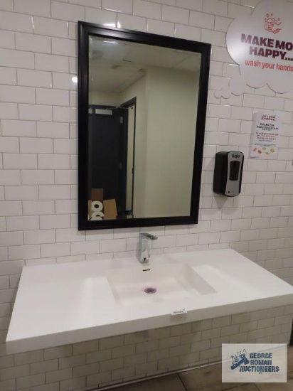 Decorative bathroom sink with black beveled mirror, soap dispenser, and two paper towels dispensers.