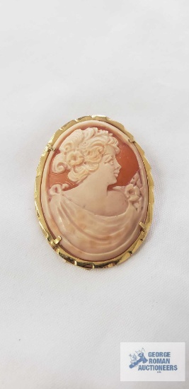 Oval Cameo brooch with a carved cream colored profile of a classical woman set in a gold tone frame,