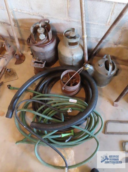Garden hoses, antique propane burners, propane tanks, barrel pump, and metal watering can.