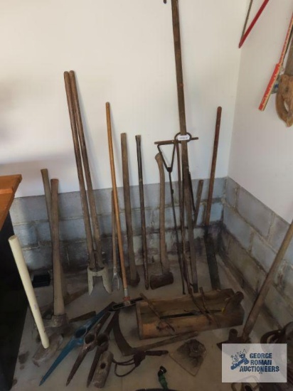 Assorted yard and garden tools including tree pruner, axe parts, post hole digger, sledgehammer,