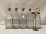 Collection of 5 printed glass liquor bottle decanters with stoppers. Labeled for Rye, Bourbon,