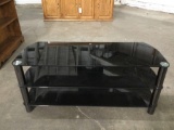 Modern black glass entertainment center / TV stand, shows some wear