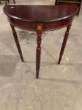 Vintage wooden side table with three legs and medallion on front.