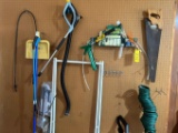 Contents of peg board: hand saw, hoses, garden tools