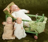 Three German bisque baby dolls resting in wooden baby bed.