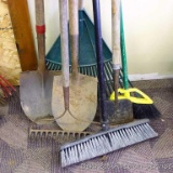 Seven yard tools incl. two brooms, garden rake, two spade shovels, leaf rake and scraper.