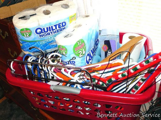 Large laundry basket filled with toilet paper, kleenex, waste basket, hangers and more. Basket is