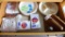 Assorted paper plates, napkins, plastic flatware, wicker plate holders, wooden napkin holder.