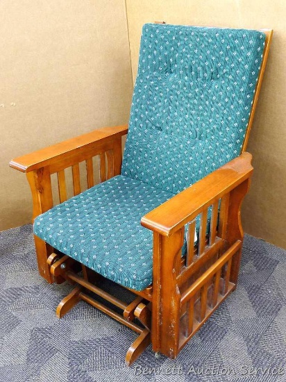 Wooden glider rocker has magazine racks on each side and appears is good condition with normal wear.