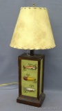 Rustic lamp with faux fishing lures, works. Lamp shade shows scene with bear. measures 25