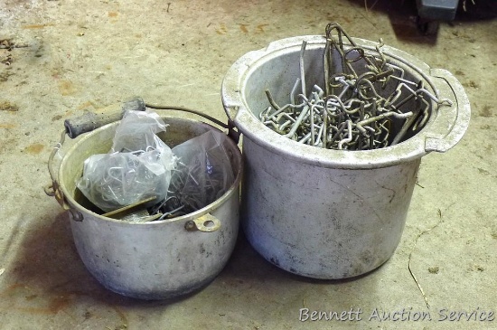 Two aluminum pails. One filled with peg board hooks. One filled with electric fence clips for