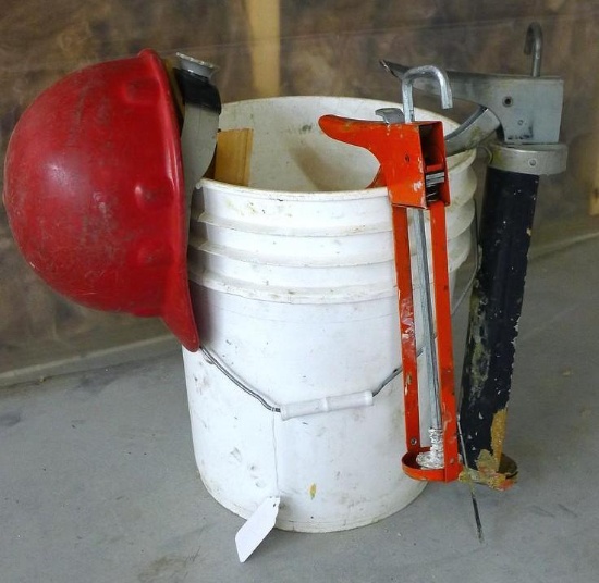 5 Gallon pail filled with wooden door shims, hard hat and 13" and 16" caulking guns.