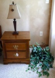 Solid wood end table with a nice little table lamp and wall hanging with faux greenery. End table is