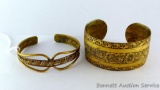 Two gold toned cuff style bracelets. Thicker cuff is 2-1/2