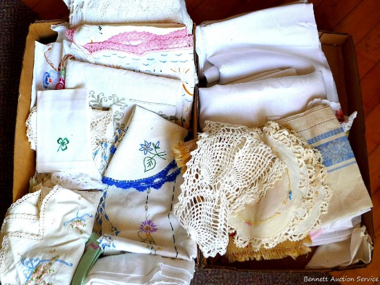 An arrangement of embroidered table runners, table cloths, decorative cloths, and doilies. One of