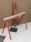 Two folding steel saw horses with a 2x4 wood top. The saw horses have are adjustable height legs.