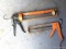 Pair of orange caulking guns. The larger gun is a heavy duty one and measures 17