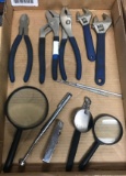 Group of pliers, adjustable wrenches magnifying glasses and magnetic bit grabber