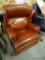 (R4) FAUX LEATHER ROCKING RECLINING ARM CHAIR. HAS BRASS STUDDING ALONG THE ARMS AND SIDES: