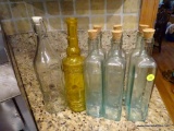 (K) GLASS BOTTLES; TOTAL OF 8, 6 CLEAR WITH CORKS, YELLOW ORNATE WITH NO CLOSURE, AND A CLEAR ROUND