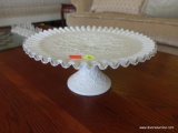 (R2) MILK GLASS PEDESTAL CAKE PLATE WITH RUFFLED EDGE AND TEXTURED PATTERN. EDGES ARE CLEAR, GIVING