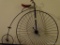 (LR) VINTAGE WROUGHT IRON BICYCLE; BLACK FRAME, RED SEAT, BIG FRONT WHEEL. MEASURES