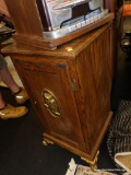 (R4) OAK STORAGE CABINET WITH BRASS OWL MEDALLION AND BRASS FEET; SINGLE PANEL DOOR WITH 1 INTERIOR