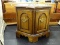 WOODEN END TABLE; HEXAGONAL SHAPED WITH 1 DOOR. MEASURES 24 IN X 22 IN. 2 DOORS ON THE FRONT OF THE