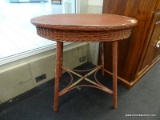 MAROON WOOD AND WICKER TABLE; OVAL SHAPED WITH WICKER APRON AND SPLAYED LEGS WITH X-STRETCHER BASE.