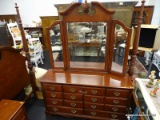 DRESSER WITH TRIFOLD MIRROR; CHERRY FINISH WOOD. TRI FOLD MIRROR IS HINGED AND HAS A BROKEN PEDIMENT