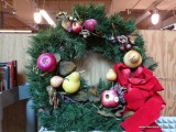 HOLIDAY WREATH; GREEN ARTIFICIAL PINE, ROUND, ACCENTED WITH APPLES AND PEARS WITH A LARGE RED BOW.